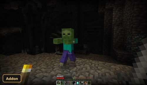 player holding a torch in a dark cave with a zombie
